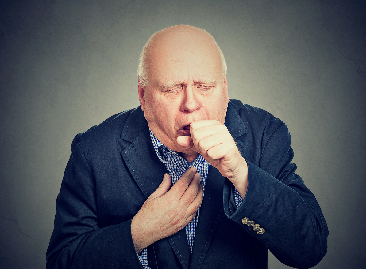 Old man coughing holding fist to mouth isolated on grey background