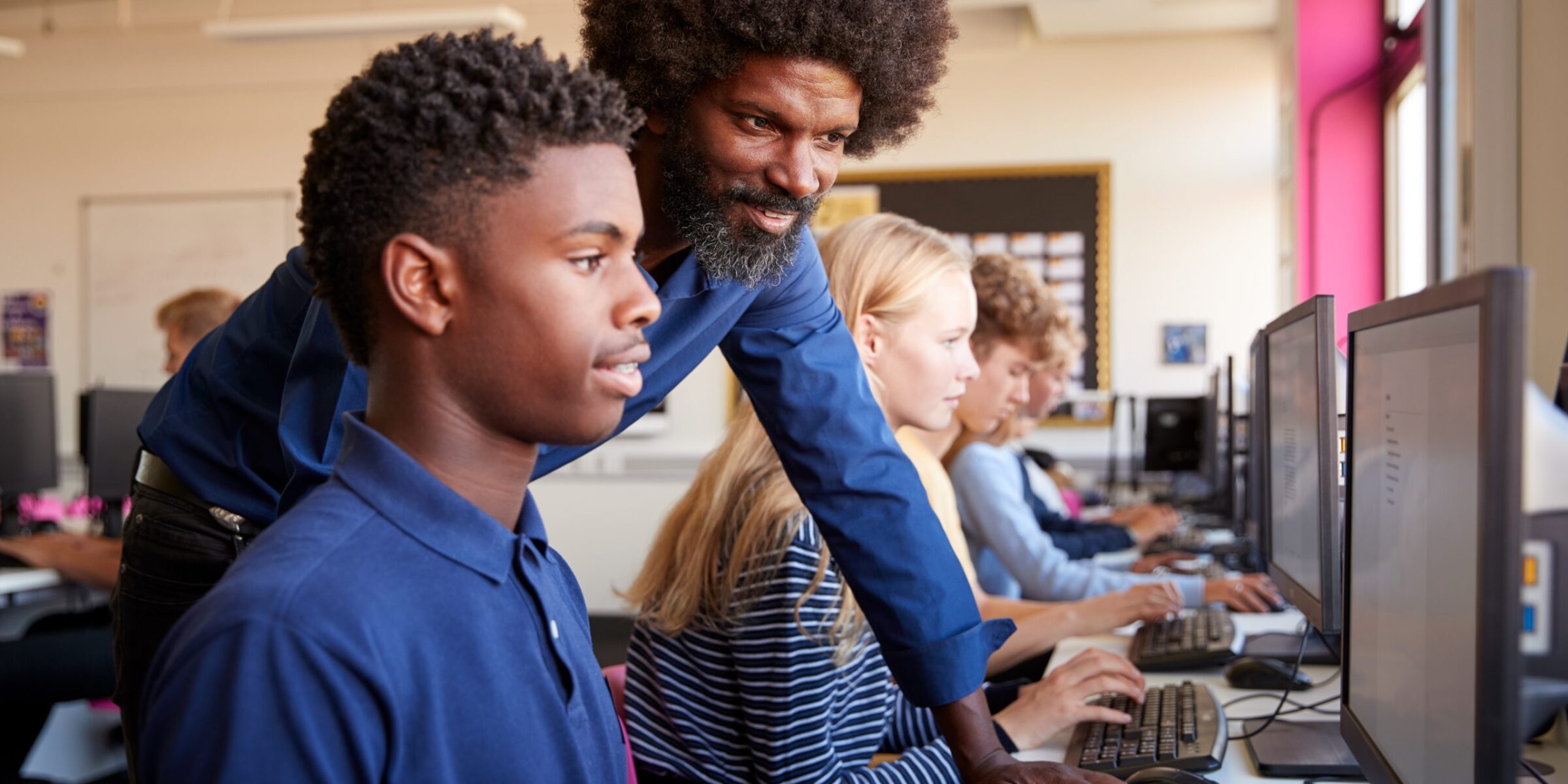 A teacher looks over a studen'ts should and assists with computer work