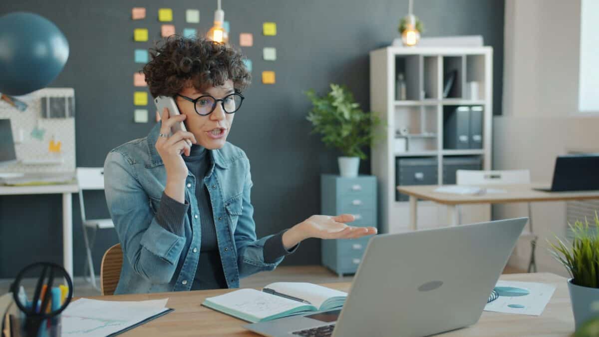 Frustrated woman on the phone with a laptop in front of her.,